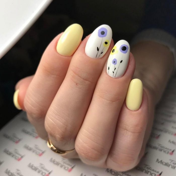 Uñas pintadas de amarillo y blanco con diseño de flores y puntos