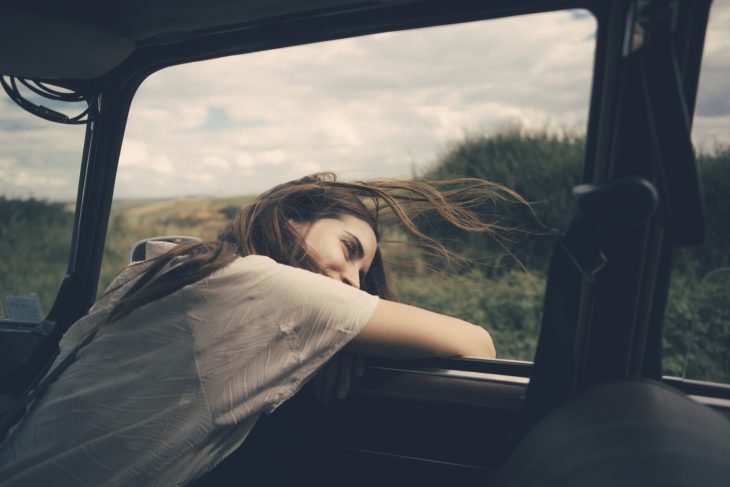 Chica de cabello castaño y despeinado mira por la ventana de un carro