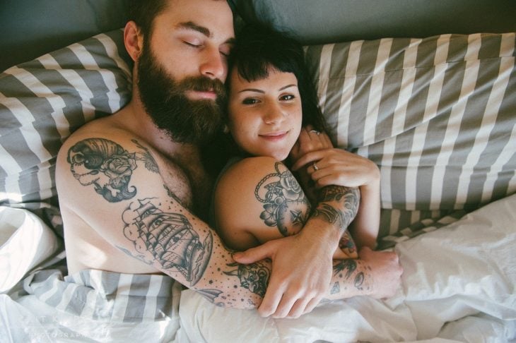 hombre blanco con barba y tatuajes abrazando a mujer 