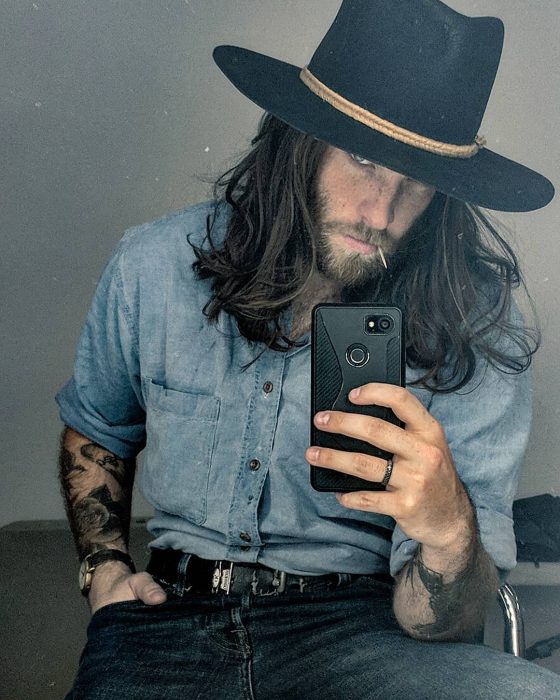 Hombre con cabello largo y barba usando sombrero y tatuajes en los brazos