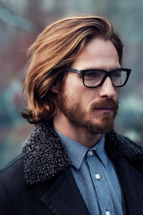 Hombre de cabello largo y castaño con barba y lentes de aumento