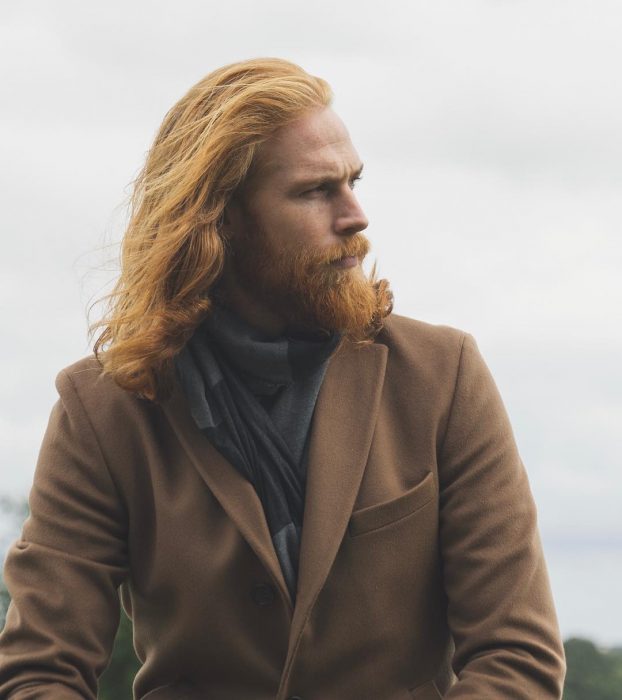 Hombre pelirrojo con barba y cabello largo usando un abrigo café