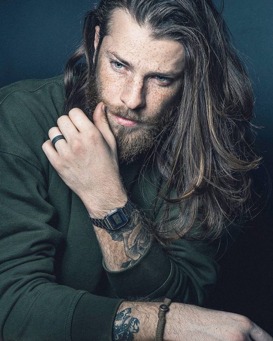 Hombre de cabello largo con barba, ojos azules y tatuajes en los brazos