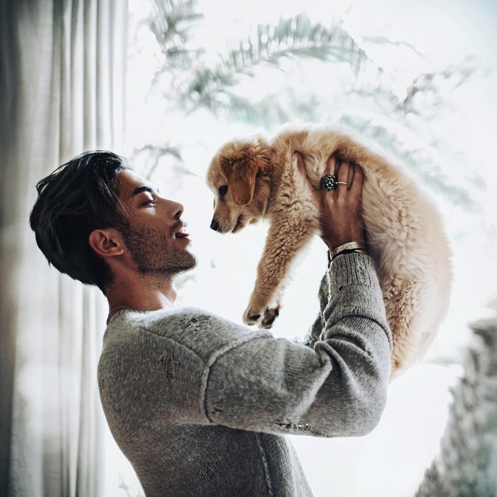 Hombre de cabello negro y barba cargando a un perrito café