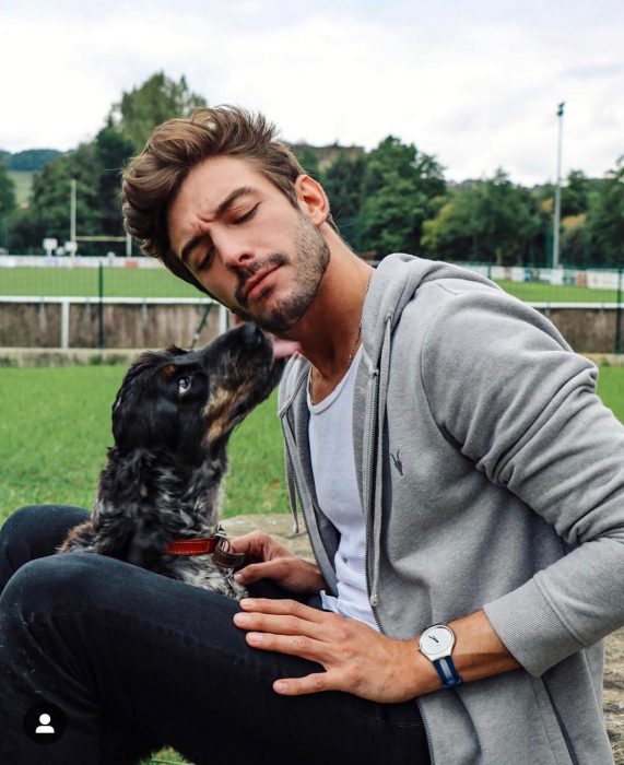 Hombre de cabello castaño con barba y un perro lamiéndole la cara