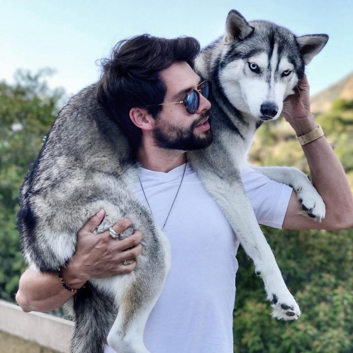 Hombre con lentes de sol cargando a un perro husky