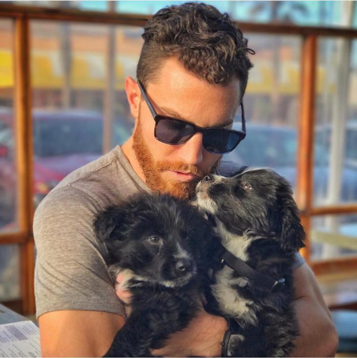 Hombre con lentes de sol cargando a dos perros cachorros