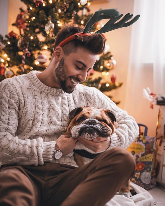 Hombre con cuernos de reno abrazando a un perro bulldog inglés