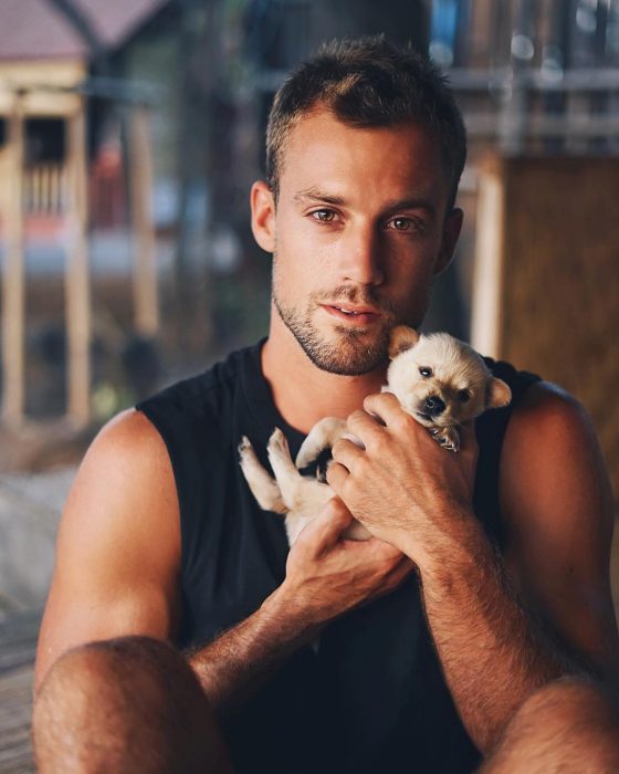 Hombre de ojos café cargando a un cachorro blanco