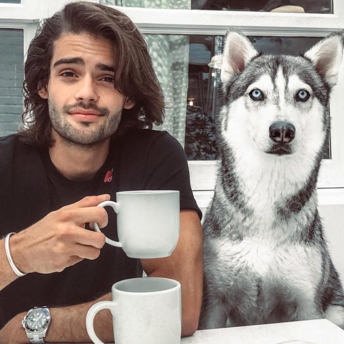 Hombre de cabello largo bebiendo café a lado de un perro husky