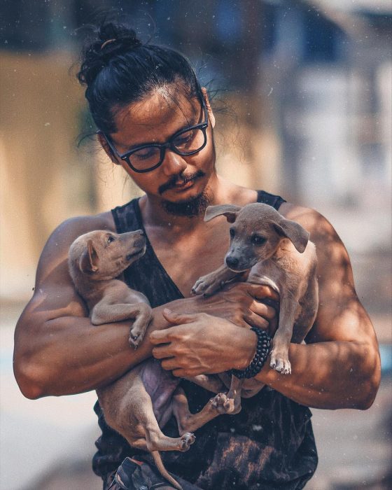 Hombre de cabello largo con chongo cargando a dos perros cafés