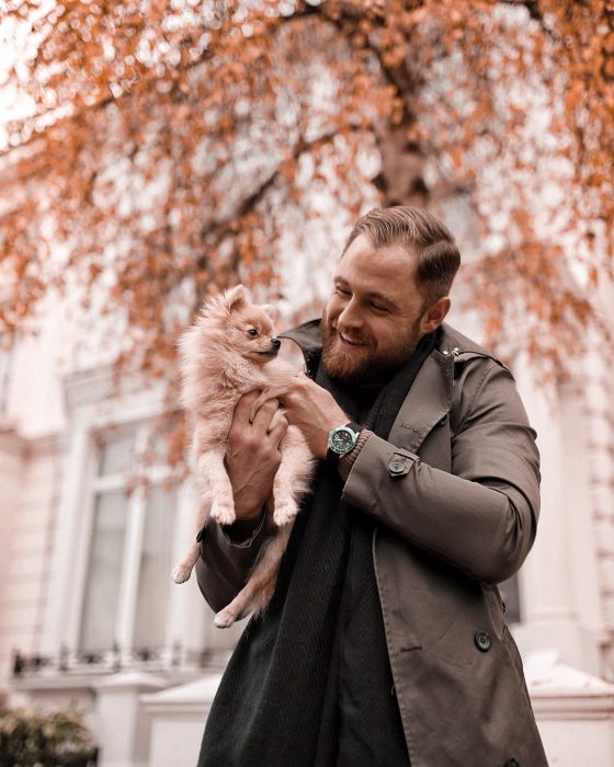 Hombre ruboi de barba cargando un perro de raza pomerania