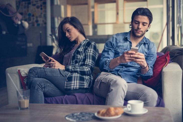 Pareja sentada en el sillón dándose la espalda y viendo sus celulares