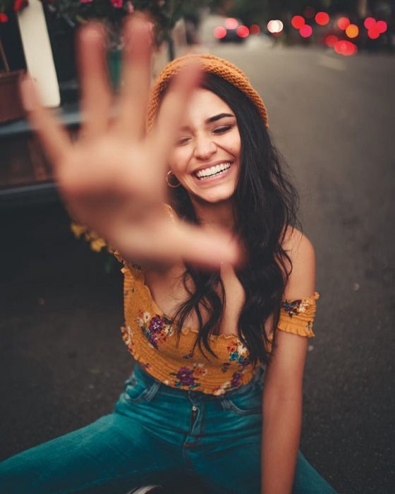 Chica con gorra anaranjada sentada en la calle sonriendo