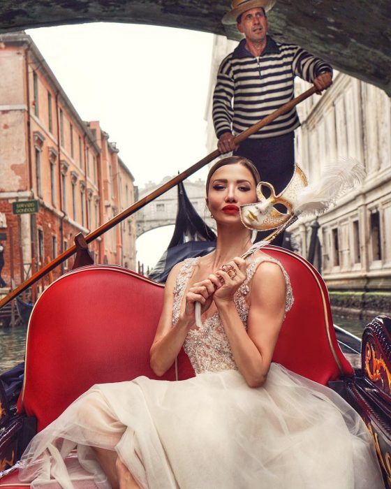 Mujer rubia con vestido blanco de tul y máscara de carnaval paseando en góndola en Venecia