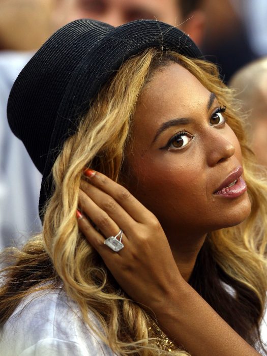 Beyonce usando un sombrero negro y tomando su cabello con las manos mientras muestra ligeramente su anillo de compromiso, un diamante cuadrado. 