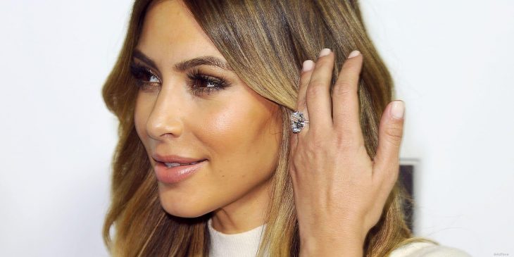 Kim Kardashian sujetando su cabello mientras muestra ligeramente su anillo de compromiso 