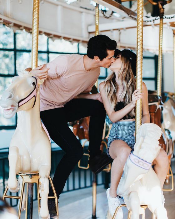 Pareja de novios besándose en un carrusel sobre caballos de juguete blancos