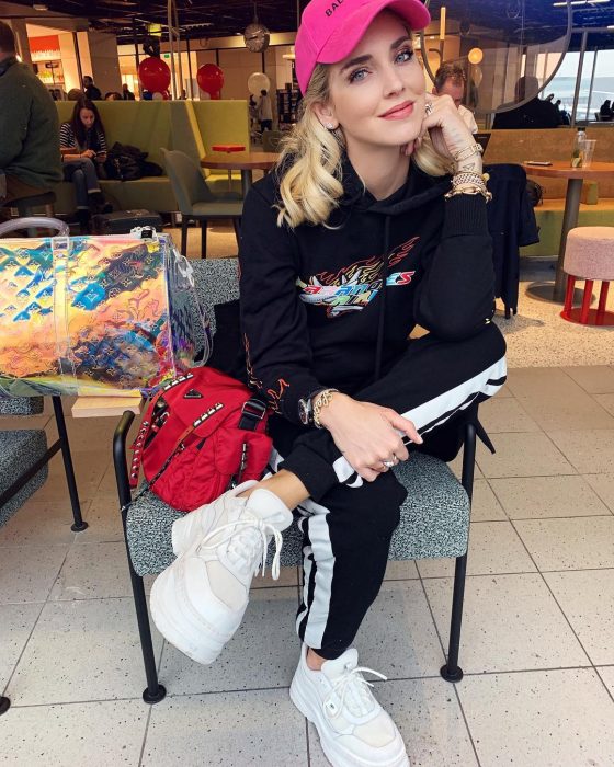 Chiara Ferragni sentada en un café usando un outfit relajado de pants, gorra rosa y tenis Fila 