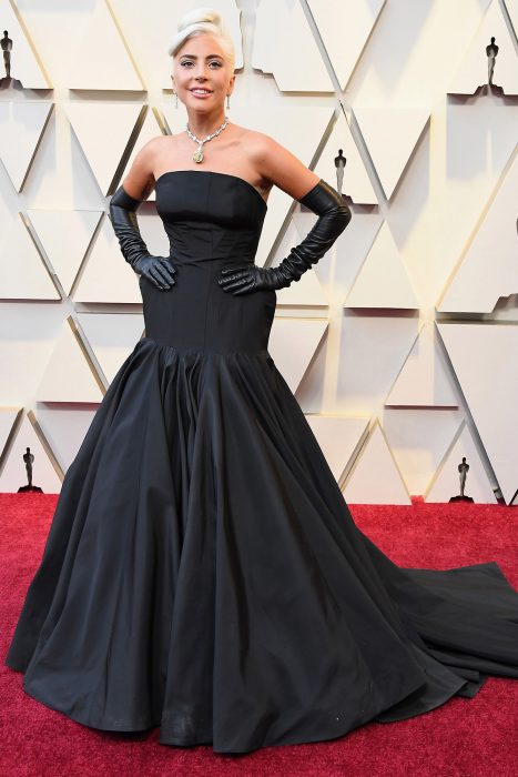 Lady Gaga usando un vestido negro de gala con guantes en la alfombra roja de los premios Óscar 2019