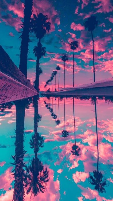 Fondo de pantalla de celular que tiene un efecto espejo de una playa con palmeras y el cielo de color azul con rosa 