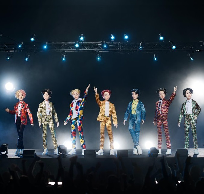 Muñecos de Mattel inspirados en el grupo musical coreano de k-Pop BTS parados en un escenario en negros y con luces azules 