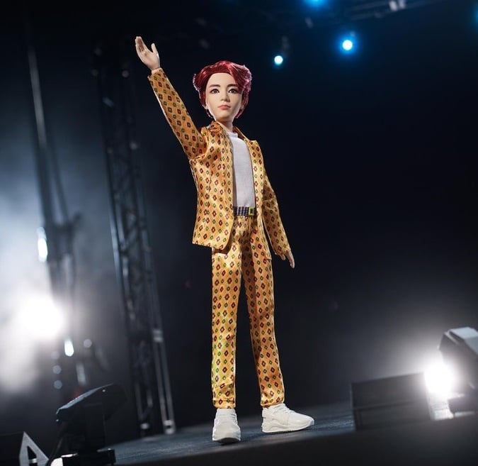 Muñeco inspirado en el cantante de la banda de K-pop, BTS, Jungkook, usando un traje amarillo con puntos de colores rojos y verdes, tenis y camisa blanca 