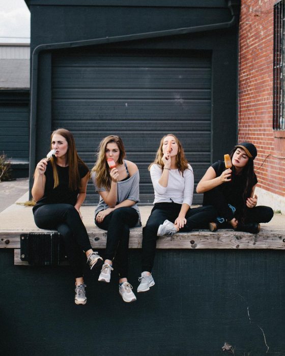 Grupo de mejores amigas sentadas en la calle comiendo una paleta helada