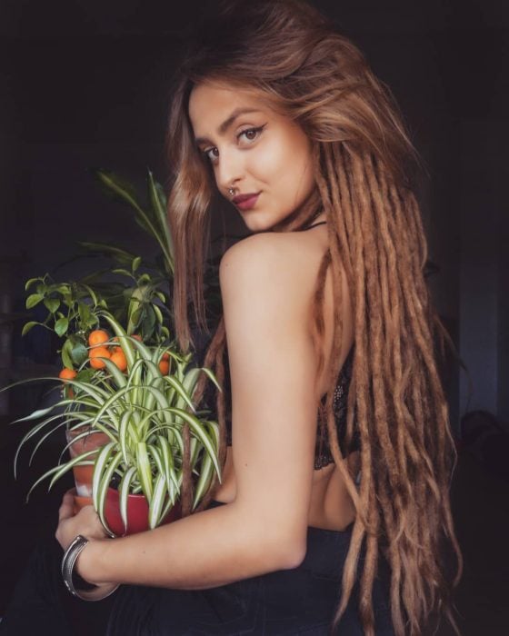 Chica con cabello largo y rastas cargando una planta