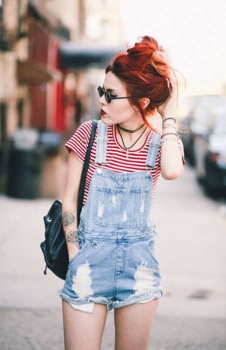 Chica de cabello rojo con overol corto y camisa a rayas blancas y rojas