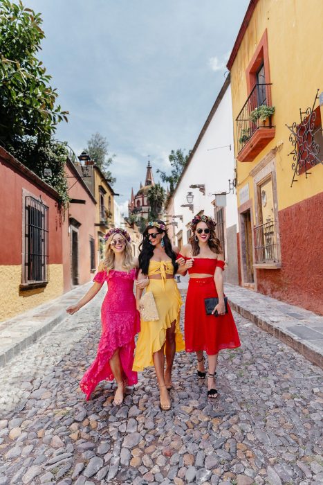 Mujeres caminando con ropa que combina y corona de flores por una calle empedrada