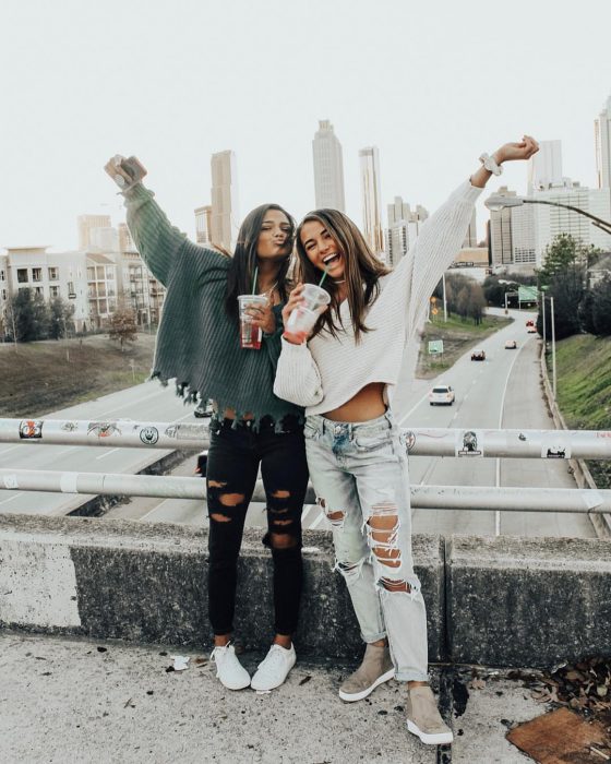 Chicas de cabello castaño en un puente bebiendo té helado con ropa que combina