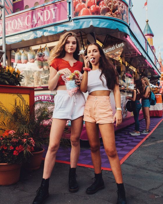 Mejores amigas en la feris comiendo algodón de azúcar usando ropa que combina