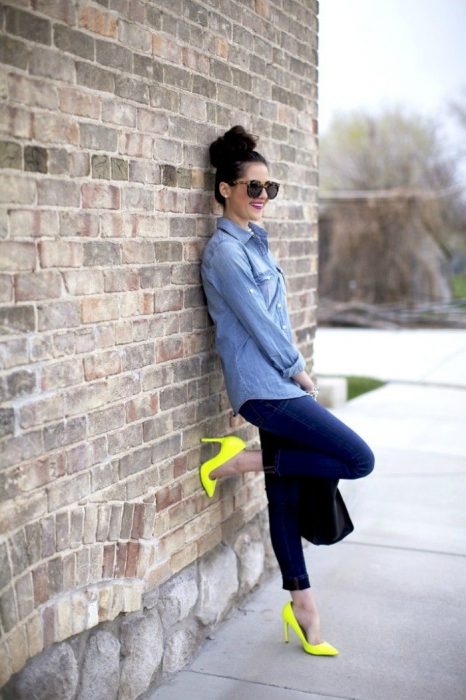 Chica con lentes de sol y tacones color neón recargada en la pared