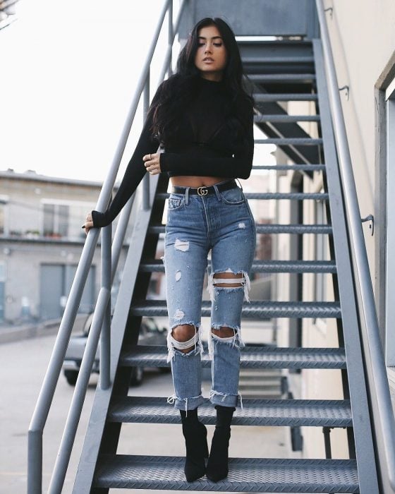 Chica en escaleras con blusa negra, jeans descastados y tacones negros