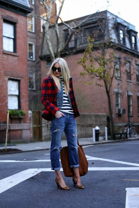 Chica rubia con abrigo de cuadros, con camisa de rayas, pantalón de mezclilla, tacones de animal print en la calle