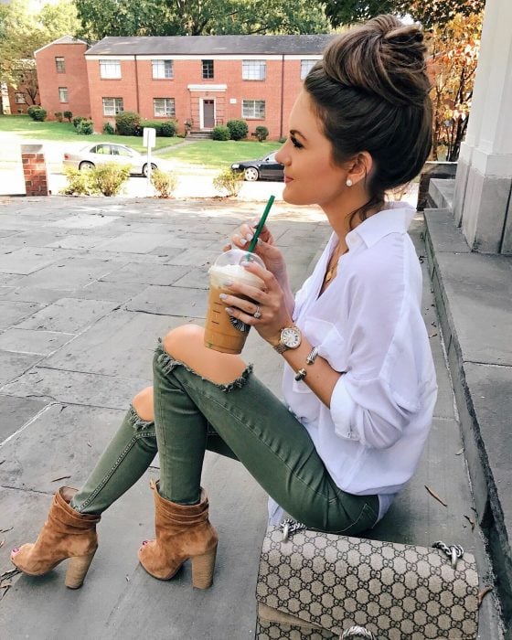 Chica sentda en escaleras bebiendo café con jeans verdes y rotos