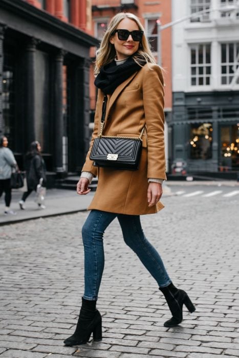 Chica rubia con saco beige, pantalones de mezclilla y tacones columna caminando en la calle