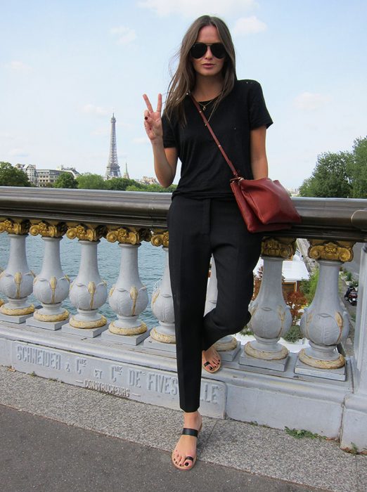 Chica posando con un atuendo negro, sandalias negras y bolso rojo quemado