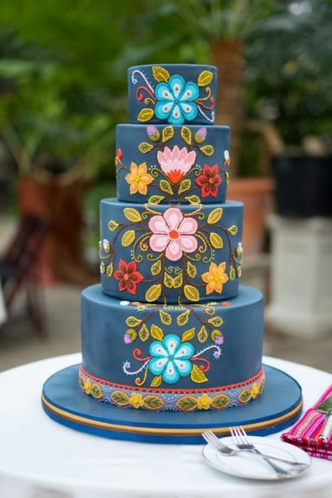 Pastel de tres pisos con betún en color azul marino y decorado de en flores de colores simulando tejido