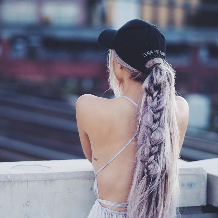 Chica de cabello color lila peinado con una trenza y usando gorra