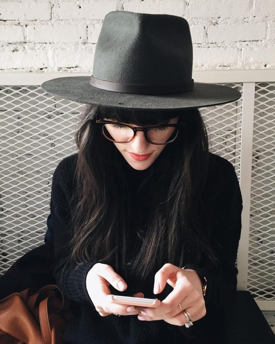 Chica con sombrero negro y lentes usando el celular