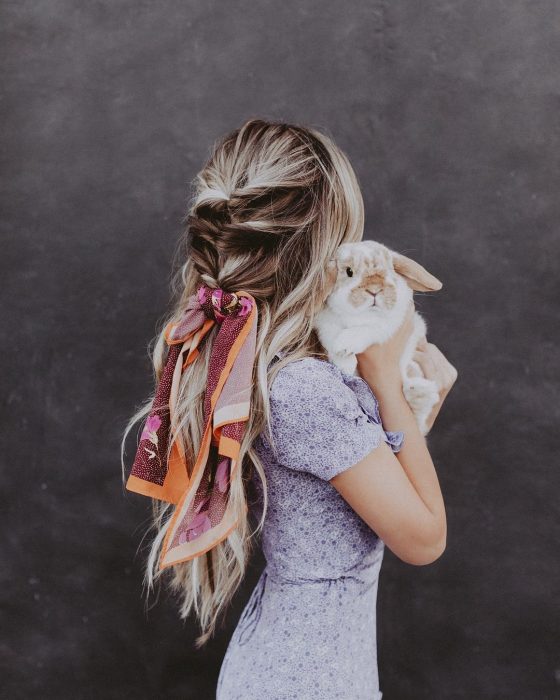 Chica rubia con trenza y bandana cargando a un conejo