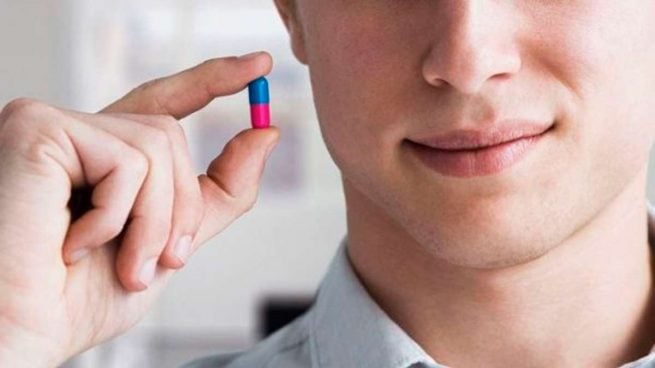 Hombre sosteniendo entre dedos pulgar e índice una píldora rosa con azul, un anticonceptivo masculino 