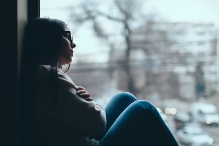 Chica con lentes triste y pensativa mira por la ventana