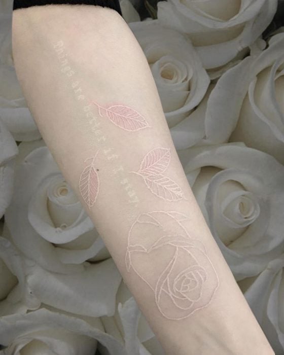 Tatuaje de tinta blanca en forma de una rosa con hojas y letras de máquina de escribir