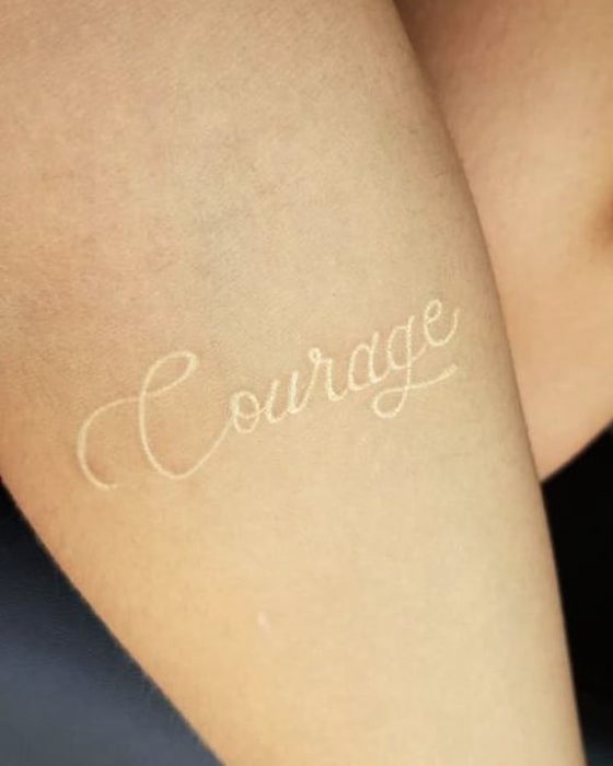 Tatuaje de tinta blanca con la palabra courage escrita en el brazo 