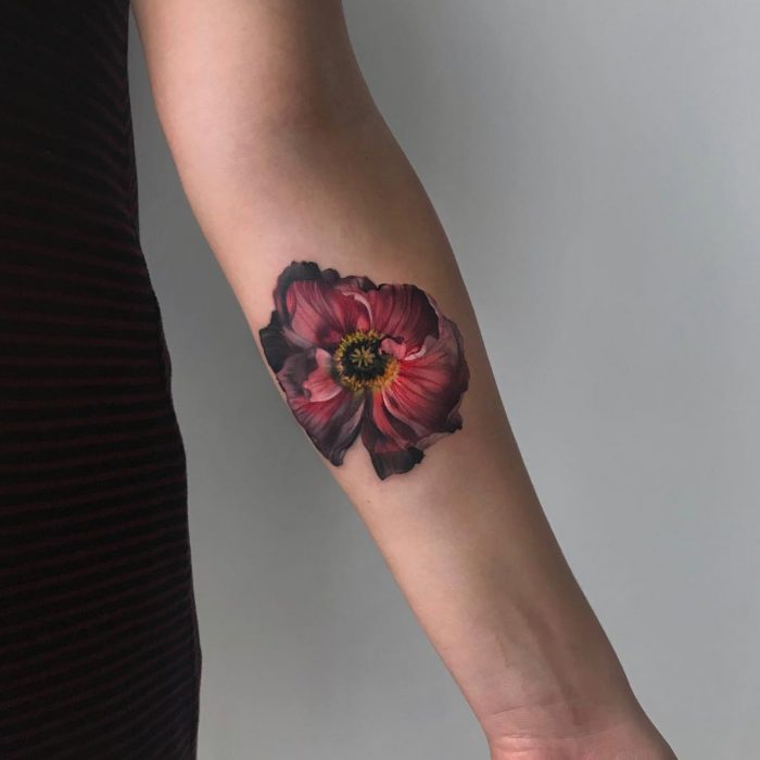 Mujer con tatuaje de flor roja realista en el brazo