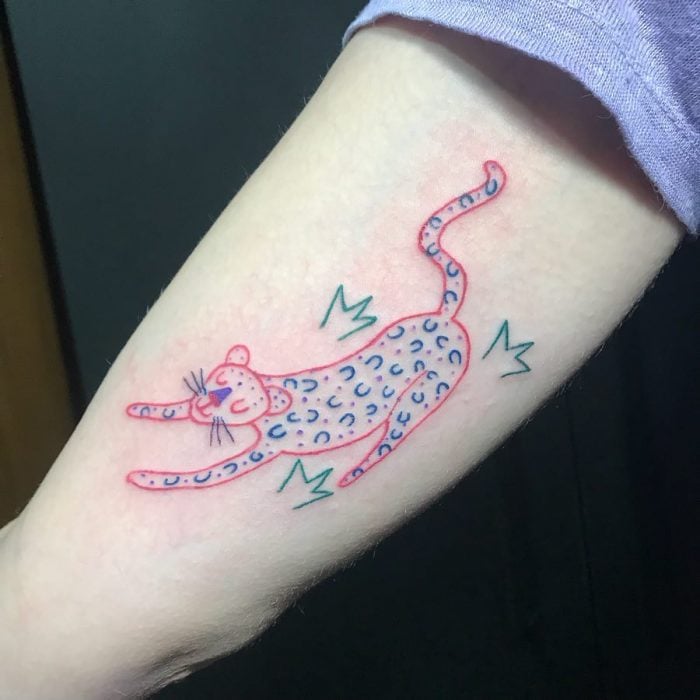Tatuaje en el brazo como dibujo infantil de un jaguar de colores hecho por la tatuadora Helen Fernandes