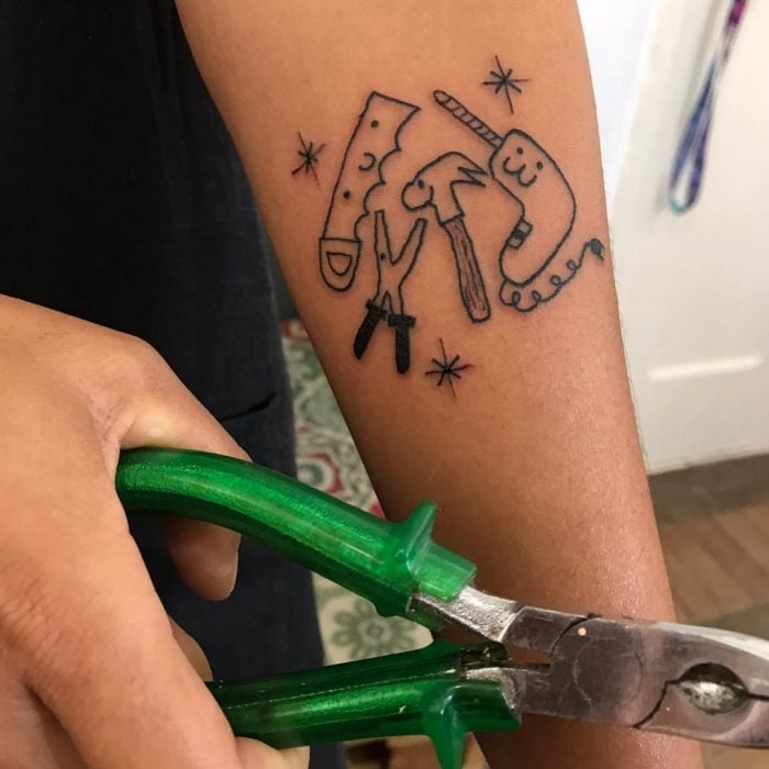 Tatuaje tierno de herramientas, serrucho, taladro, pinzas y martillo con caritas felices hecho por la tatuadora Helen Fernandes